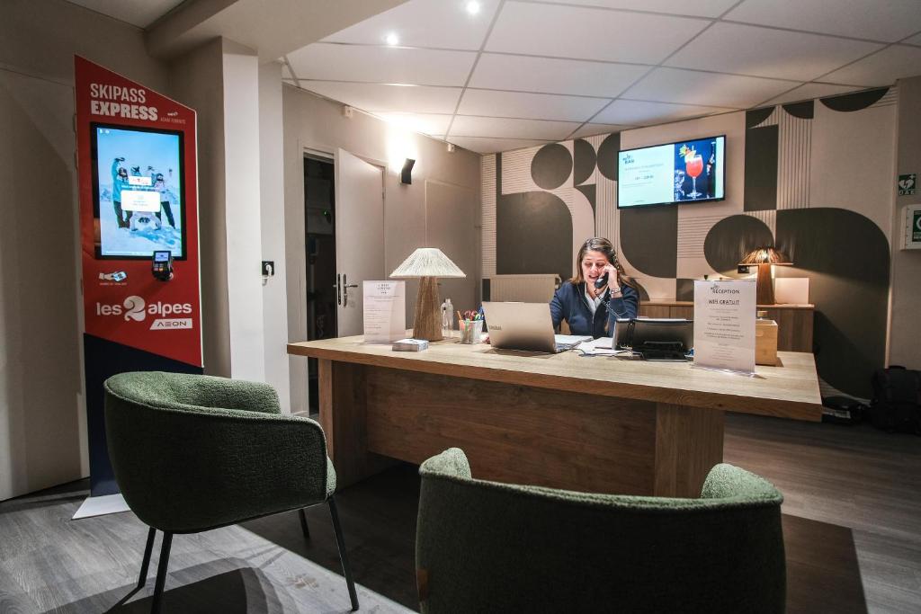 une femme parlant au téléphone portable à la réception dans l'établissement Hôtel Les 2 Alpes L'Orée Des Pistes, à Les Deux Alpes