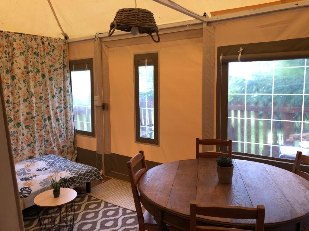 une salle à manger avec une table, des chaises et des fenêtres dans l'établissement Les lodges de phanou Tente lodge, à Prissac