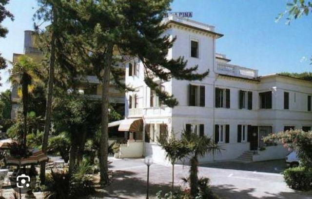 un grand bâtiment blanc avec des arbres devant lui dans l'établissement Hotel VILLA PINA, à Senigallia