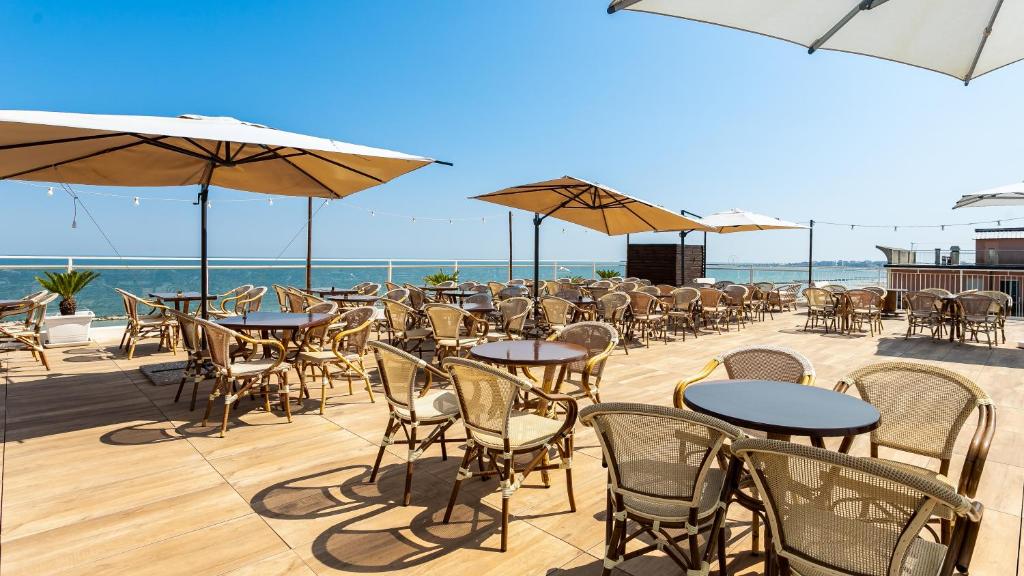 une rangée de tables et de chaises avec des parasols et l'océan dans l'établissement Hotel Blumen, à Rimini