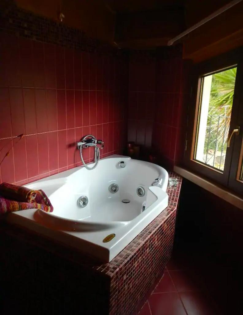 La salle de bains carrelée de rouge est pourvue d'une baignoire et d'une fenêtre. dans l'établissement Villa Migi, à Archi