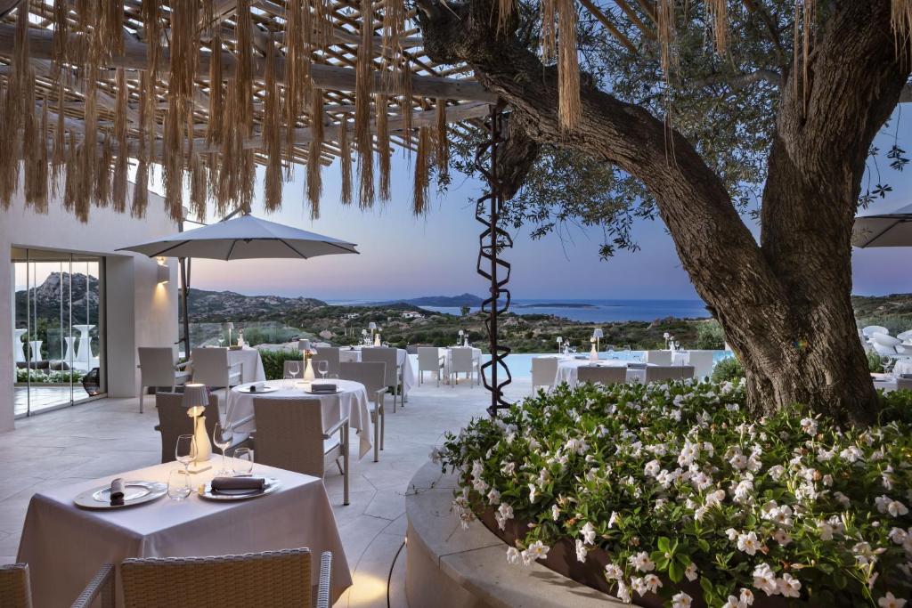un restaurant avec des tables blanches et un arbre dans l'établissement Hotel Li Finistreddi, à Cannigione