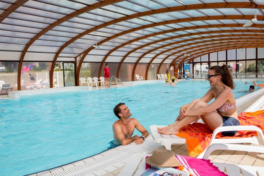 un homme et une femme assis dans une piscine dans l'établissement Mobil home Céleste 6-8 personnes, à Litteau