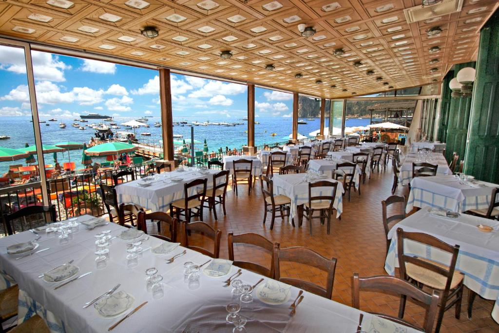 un restaurant avec des tables et des chaises blanches et l'océan dans l'établissement Hotel La Certosa, à Massa Lubrense