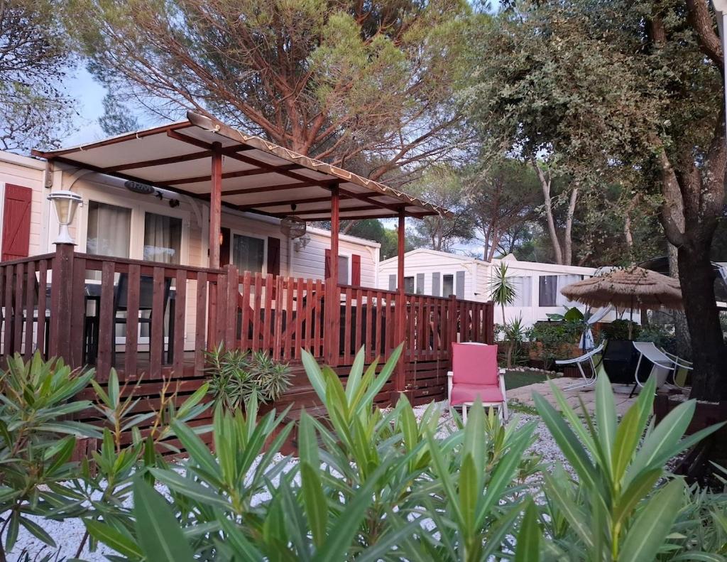 une maison avec une terrasse en bois et une chaise rose dans l'établissement Mobilhome paisible et verdoyant, à Puget-sur Argens