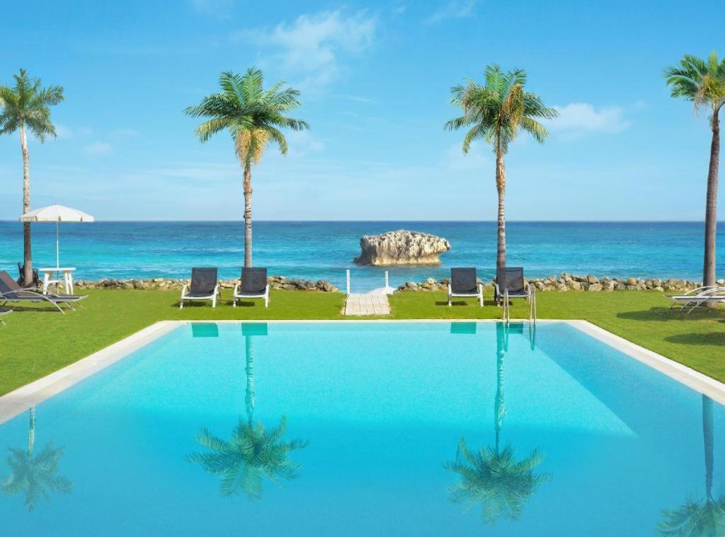une piscine avec des palmiers et l'océan dans l'établissement Borgo di Riaci Beach Resort, à Santa Domenica