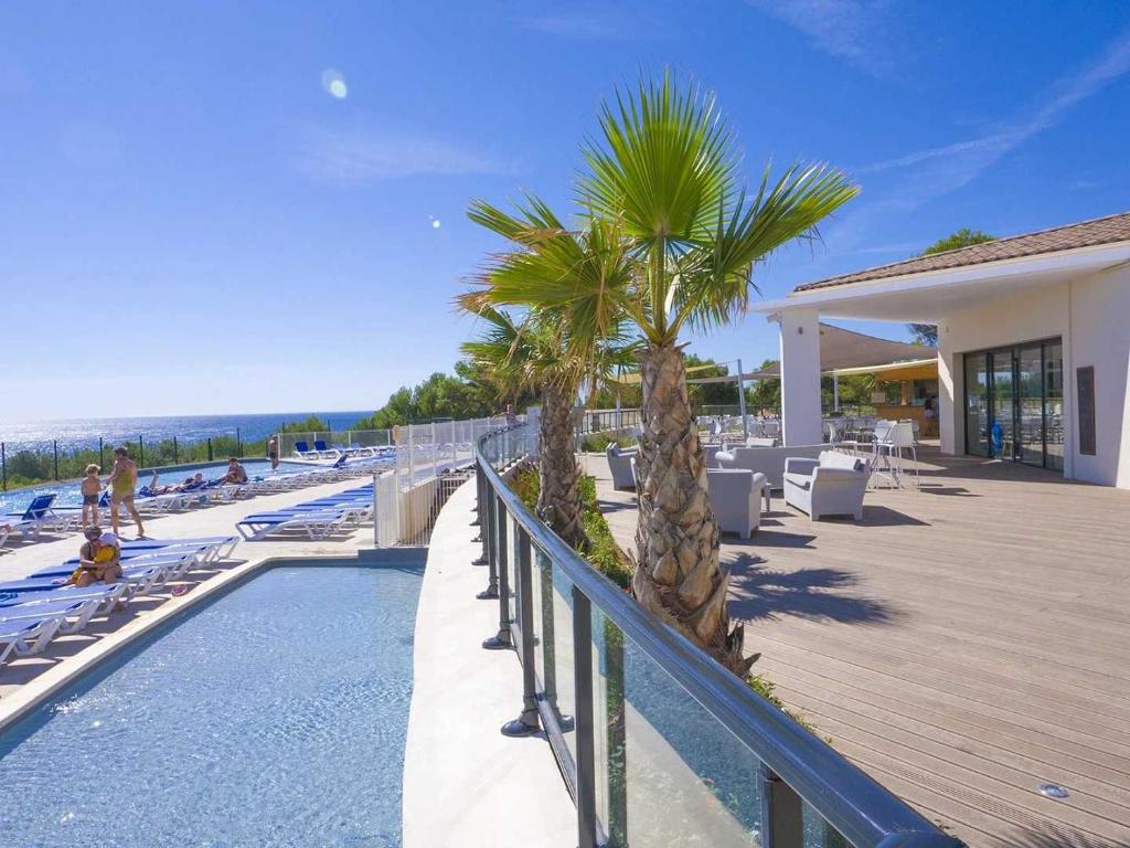 un complexe avec une piscine et une terrasse bordée de palmiers dans l'établissement Camping 4 étoiles - Parc aquatique - ef0bdc, à Martigues