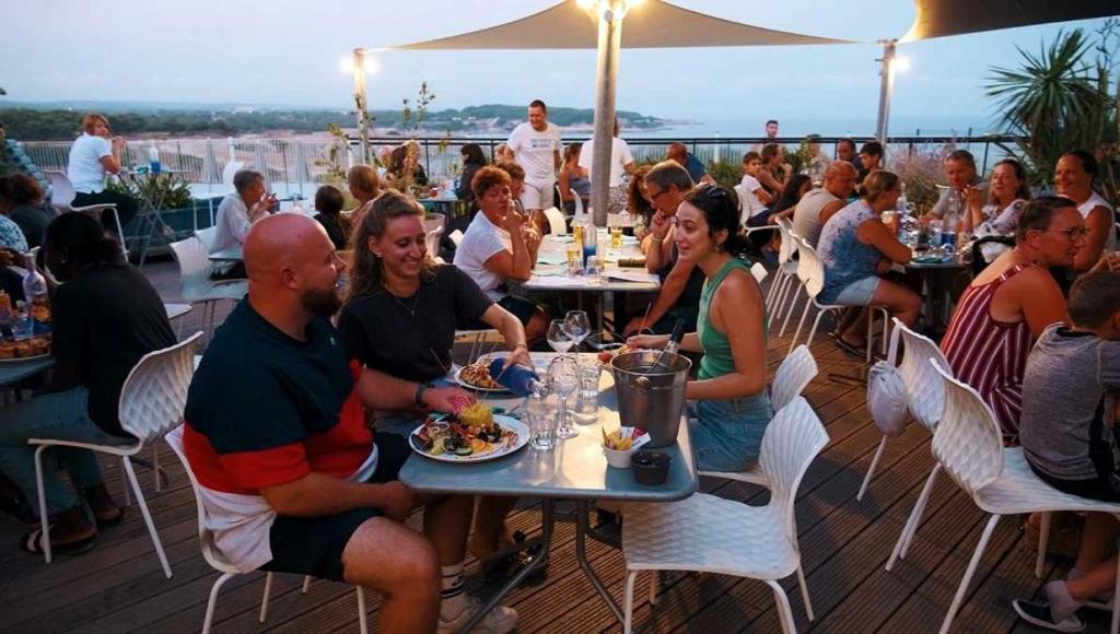 un groupe de personnes assises à des tables mangeant de la nourriture sur un toit dans l'établissement Camping 4 étoiles - Parc aquatique - ef0bdc, à Martigues