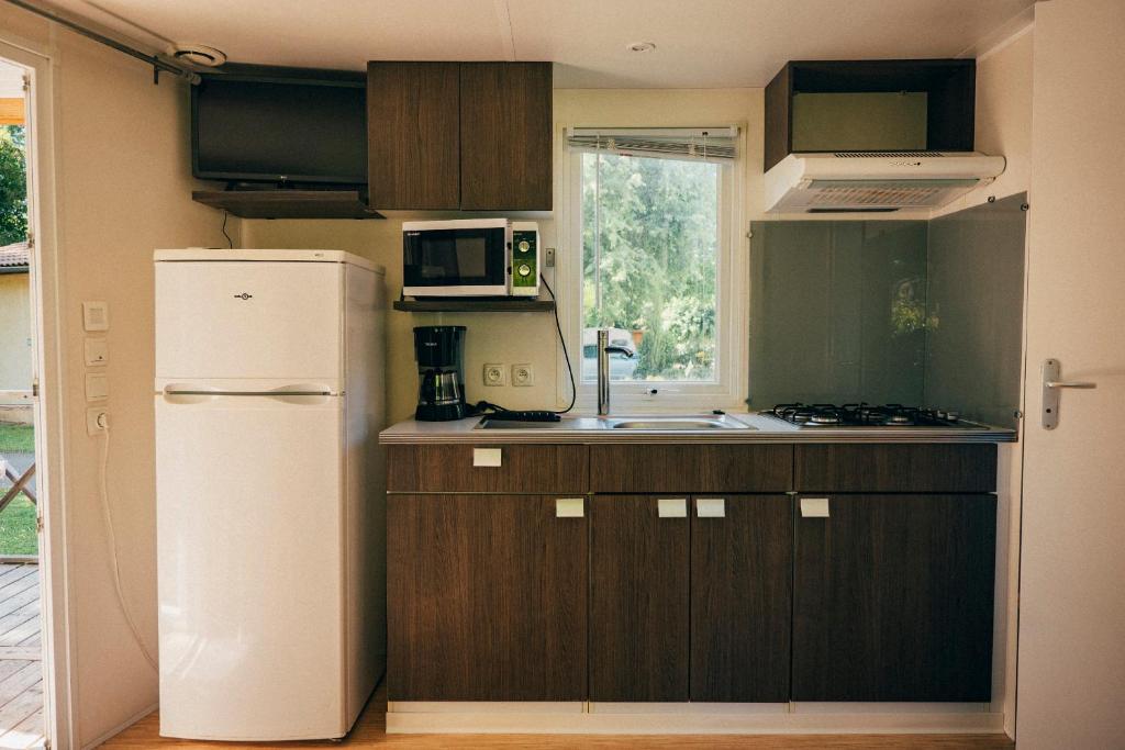 La cuisine est équipée de placards bruns et d'un réfrigérateur blanc. dans l'établissement Camping intercommunal de Beaurepaire, à Beaurepaire