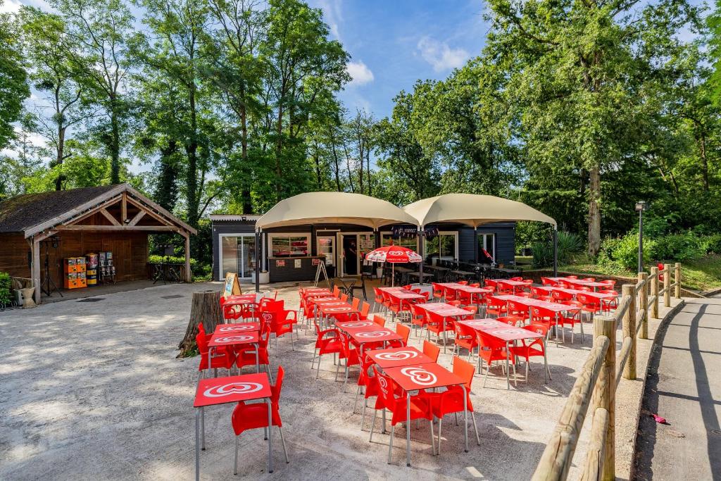 un groupe de tables et de chaises rouges devant un bâtiment dans l'établissement Camping Parc des Roches, à Saint-Chéron