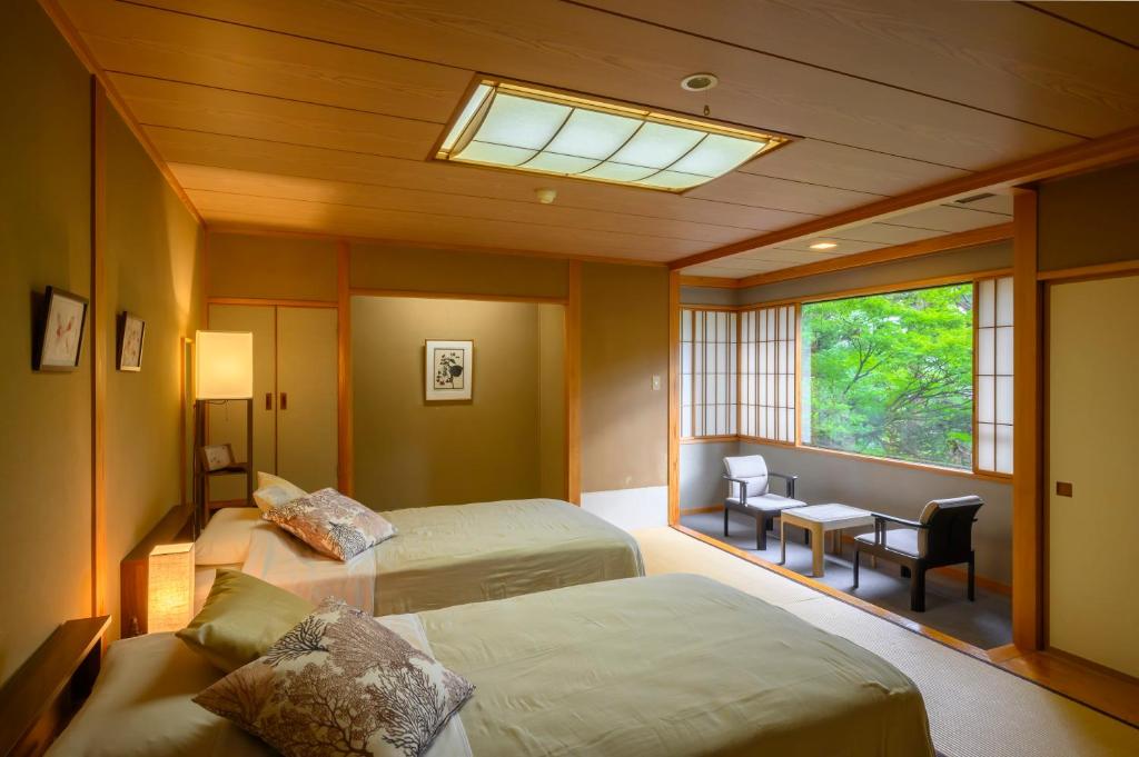 une chambre avec deux lits et une fenêtre et un bureau dans l'établissement Senkeien Tsukioka Hotel, à Kaminoyama