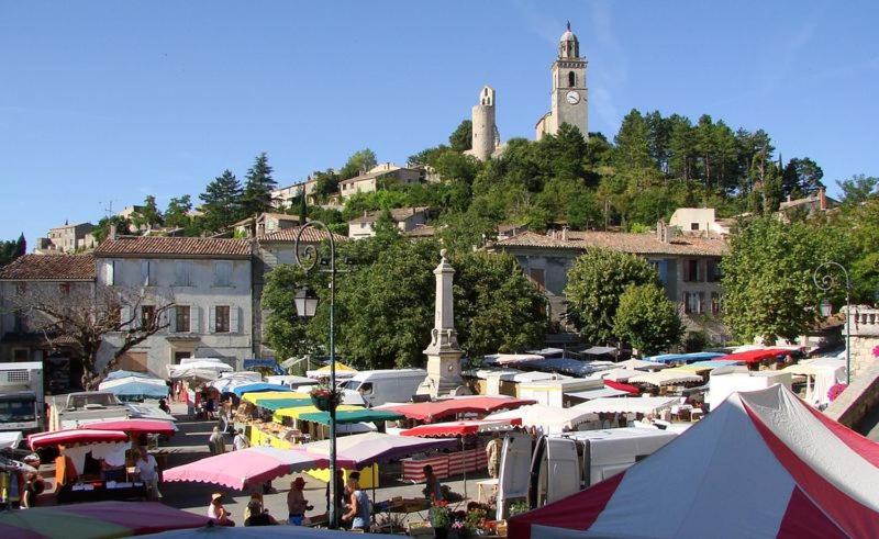 un marché avec de nombreuses tentes et une tour d'horloge sur une colline dans l'établissement Gîte Hanna en Luberon - Le Boisset de St Martin de Castillon, à Saint-Martin-de-Castillon