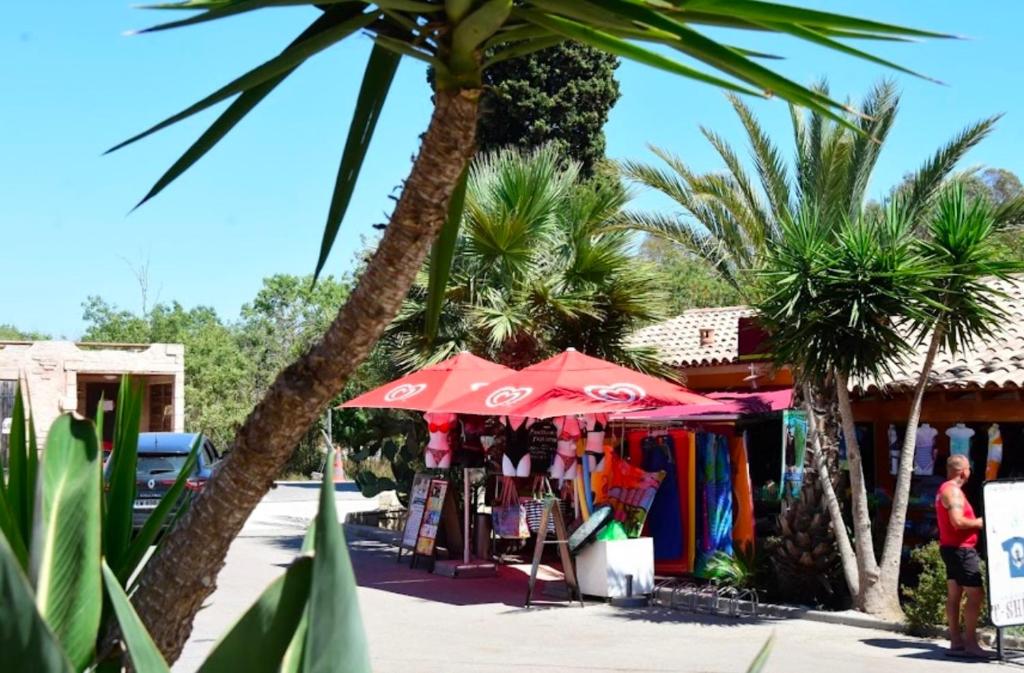 un magasin avec un parasol rouge et des palmiers dans l'établissement Mobil-home neuf 6 à 8 pers au Camping Les Palmiers, Hyères, à Hyères