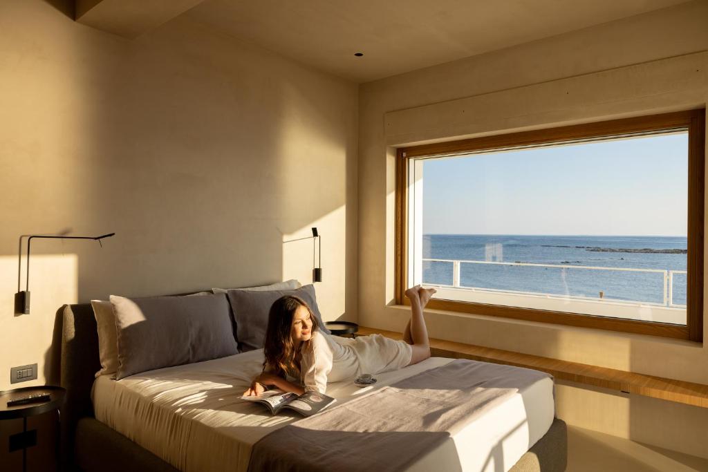 une petite fille assise sur un lit dans une chambre avec une fenêtre dans l'établissement Calitro Mare, à Torre Ovo