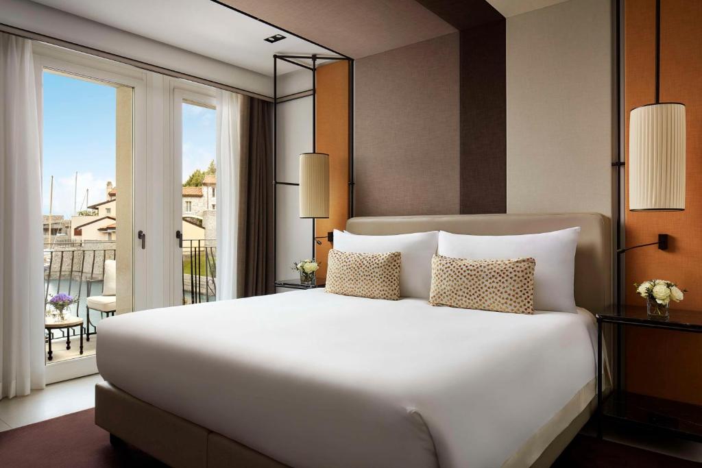 une chambre avec un grand lit blanc et un balcon dans l'établissement Tivoli Portopiccolo Sistiana Wellness Resort & Spa, à Sistiana