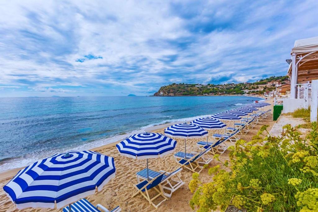 une rangée de parasols bleus et blancs sur une plage dans l'établissement Hotel Ipomea Club, à Capo Vaticano