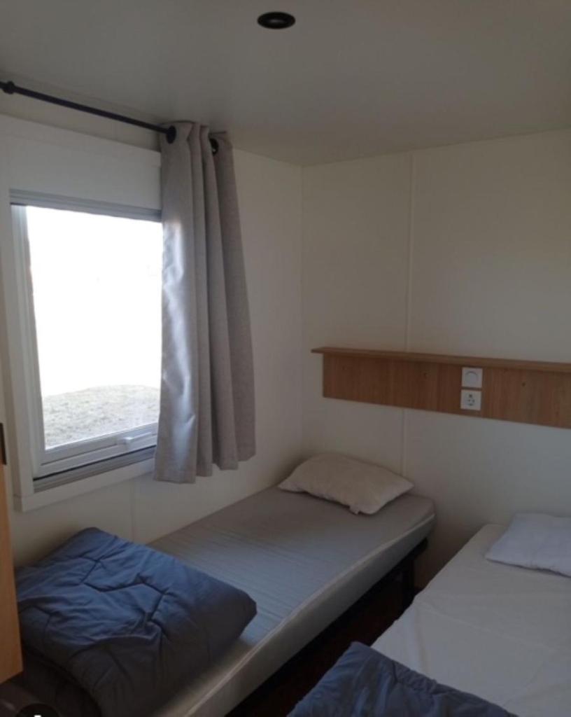 une petite chambre avec deux lits et une fenêtre dans l'établissement Mobil home Céleste 6-8 personnes, à Litteau 17 autres photos