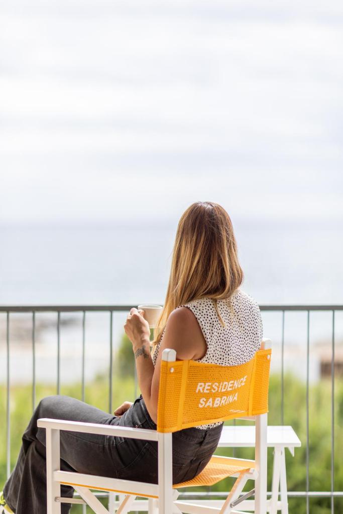 une femme assise sur une chaise regardant l'océan dans l'établissement Residence Sabrina, à Ceriale