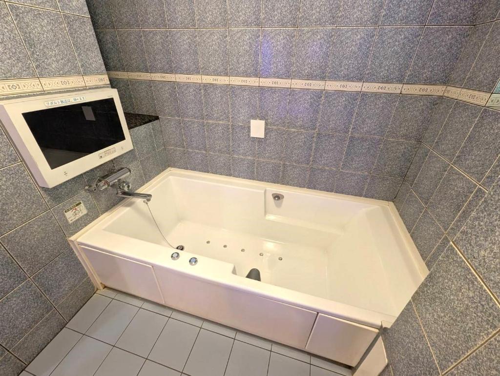 une baignoire blanche dans une salle de bain avec une télévision dans l'établissement ホテル ニューパレス, à Amagasaki