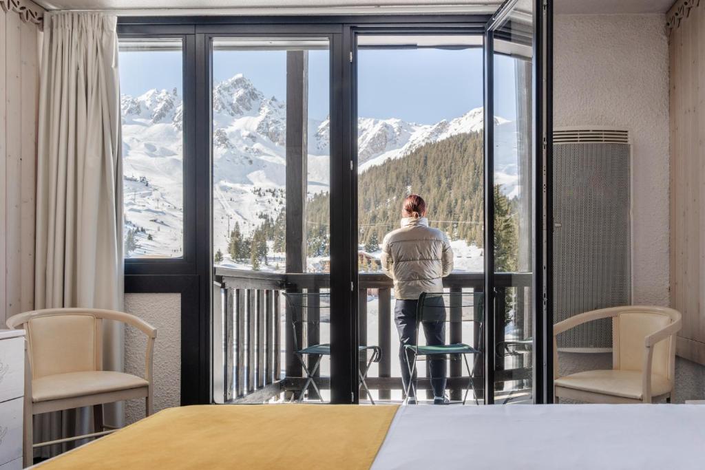 une femme qui regarde par la fenêtre d'une pièce avec vue dans l'établissement Lake Hotel Courchevel 1850, à Courchevel