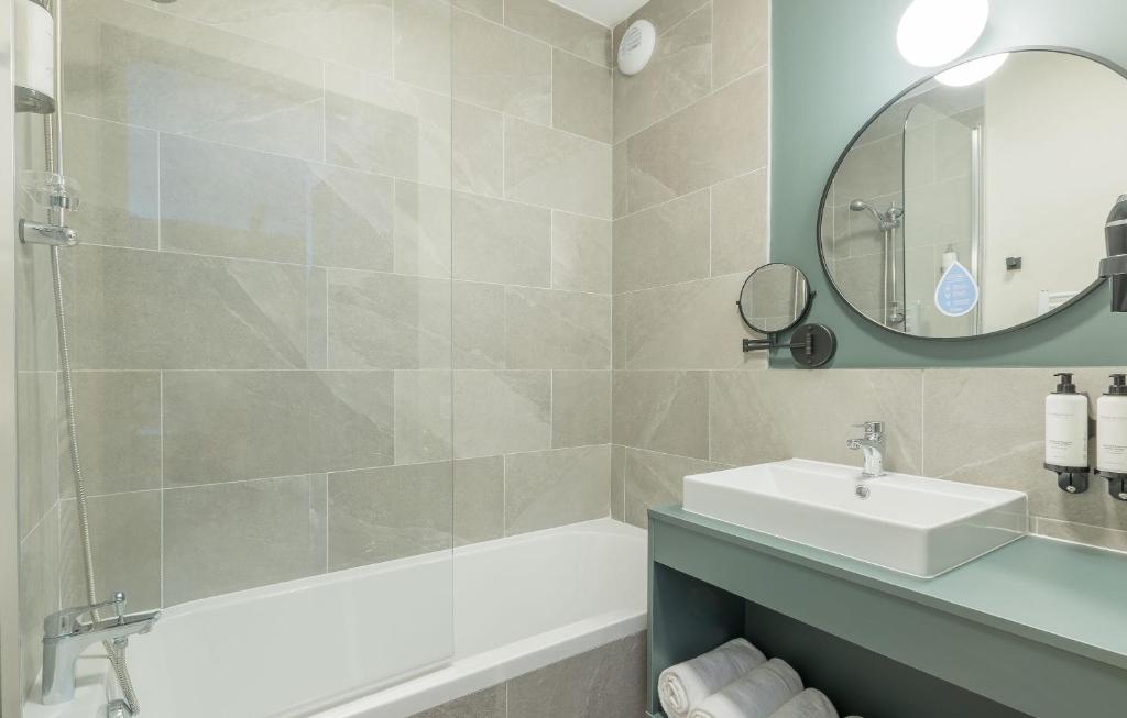 une salle de bain avec un lavabo, une baignoire et un miroir dans l'établissement Résidence Odalys L'Ecrin de Vars, à Vars