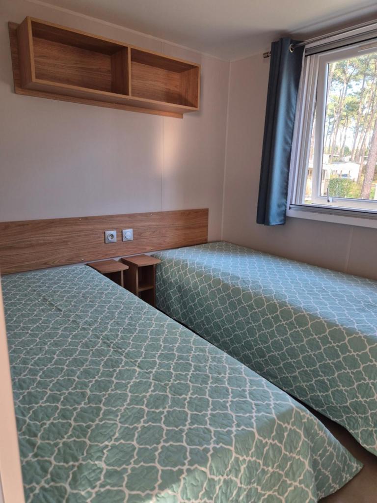 une chambre avec deux lits et une fenêtre dans l'établissement MH 201 AGREABLE et tout ÉQUIPÉ 2CH dont suite parentale et 2sdb avec vue sur foret dans camping 4 étoiles, à Saint-Julien-en-Born 23 autres photos