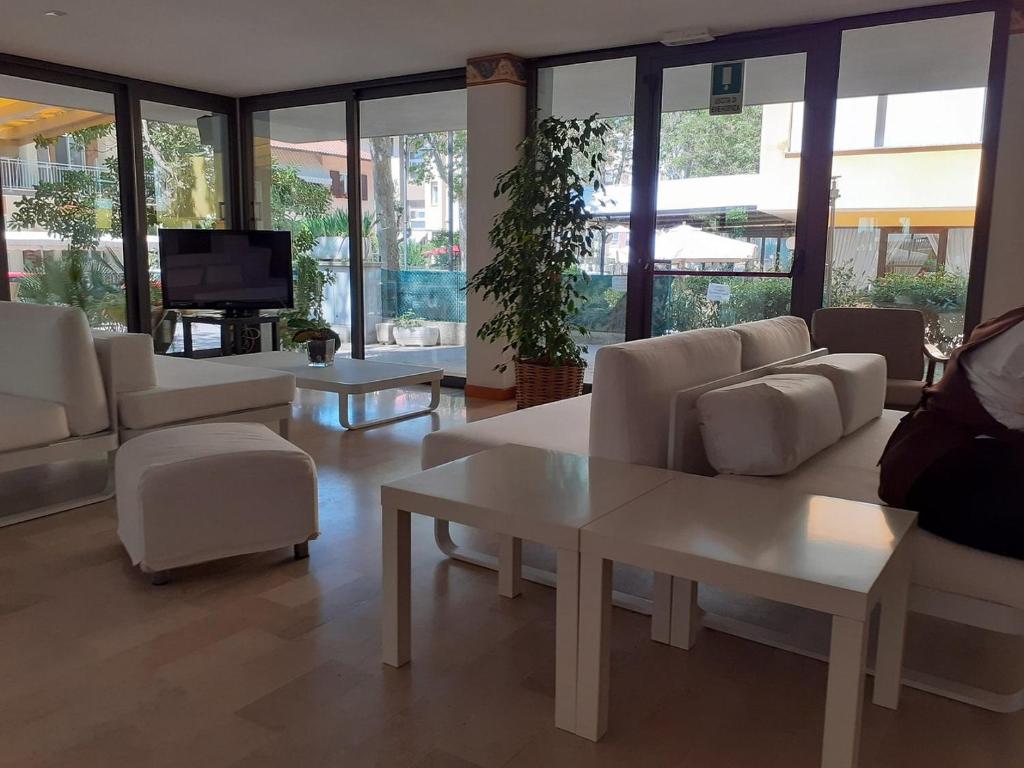 un salon avec des meubles blancs, une télévision et des fenêtres dans l'établissement Hotel Ambasciata, à Cesenatico