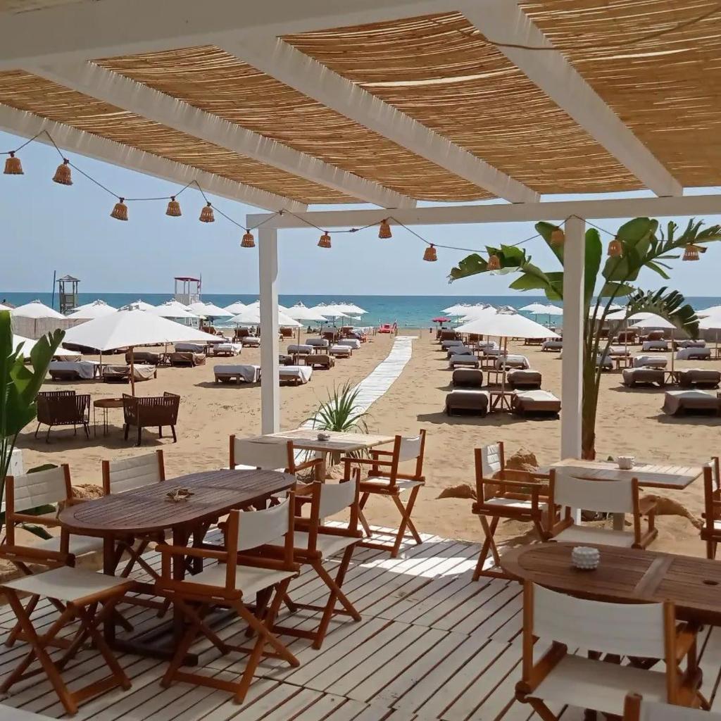 - une terrasse en bois avec des tables et des chaises sur la plage dans l'établissement Hotel Noto Marina Vista Mare, à Noto Marina