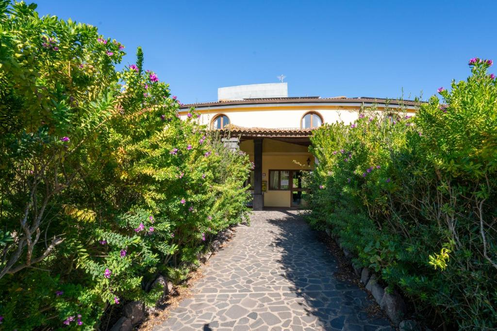 une allée menant à une maison avec des buissons et des fleurs dans l'établissement Horse Country Resort Congress & Spa - Hotel Medar, à Arborea