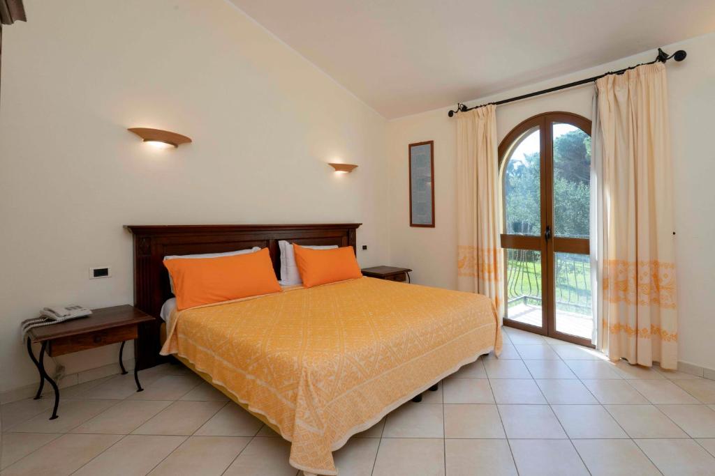une chambre avec un lit avec des oreillers orange et une fenêtre dans l'établissement Horse Country Resort Congress & Spa - Hotel Medar, à Arborea