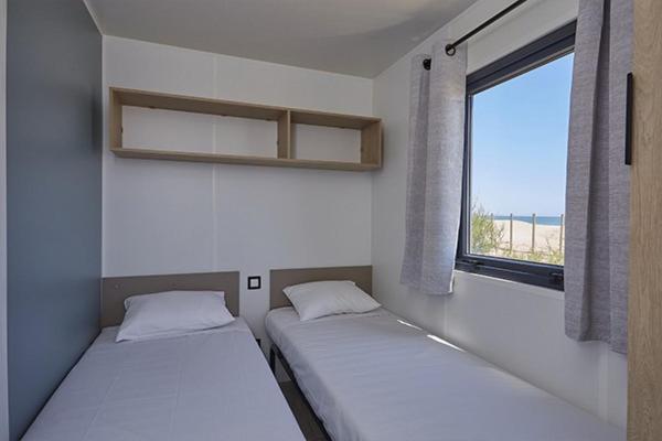 deux lits dans une petite pièce avec une fenêtre dans l'établissement Camping Les Gorges de Provence, à Saint-Laurent-du-Verdon