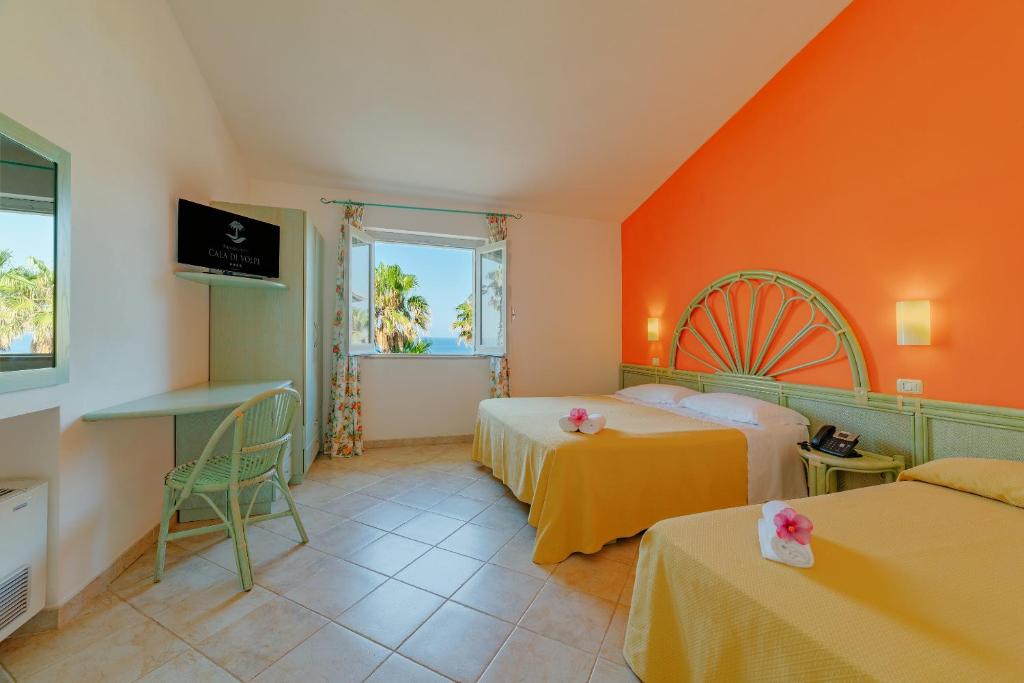 Cette chambre comprend 2 lits et un mur orange. dans l'établissement Hotel Villaggio Cala Di Volpe, à Capo Vaticano