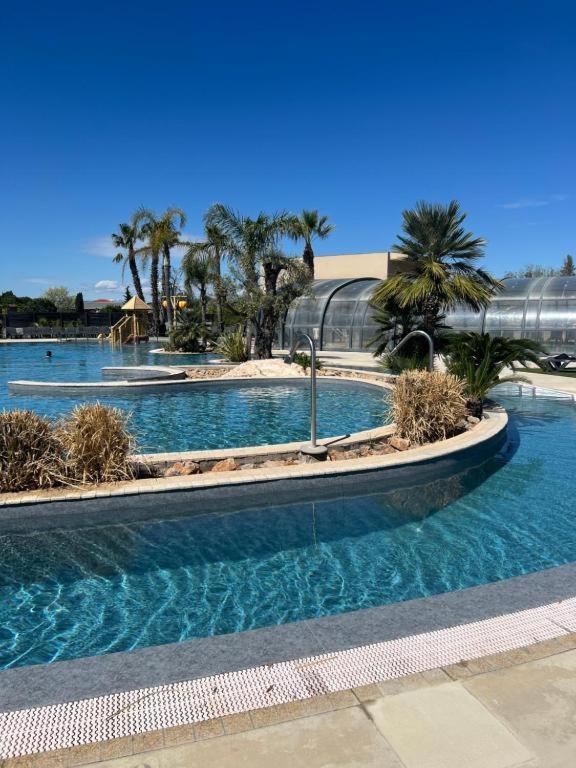 une grande piscine avec des palmiers et un bâtiment dans l'établissement Camping 5 Les Dunes Mobil-Home 6Pers, à Torreilles