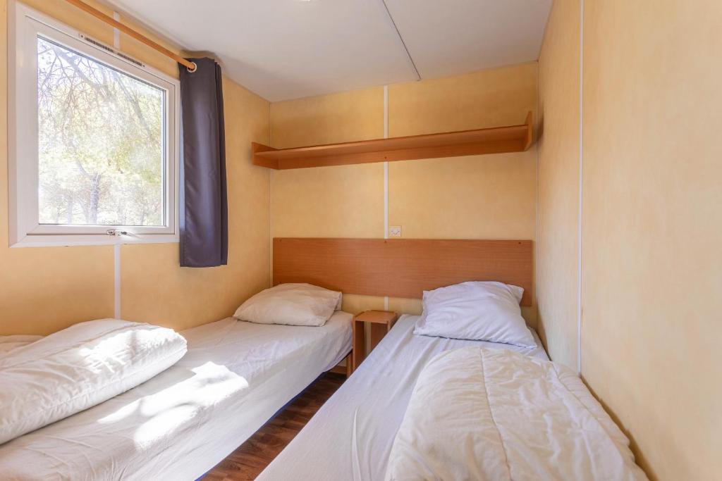 deux lits dans une chambre avec une fenêtre dans l'établissement Mobilhome Oasis village Puget, à Puget-sur Argens