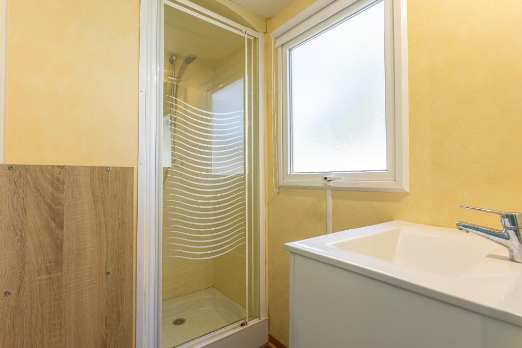 La salle de bains est pourvue d'un lavabo, d'une douche et d'une fenêtre. dans l'établissement Mobilhome Oasis village Puget, à Puget-sur Argens