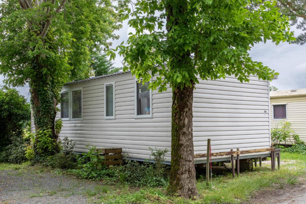 une maison blanche avec un banc à côté d'un arbre dans l'établissement Mobil-home 3 chambres - A, à Saint-Jean-de-Monts
