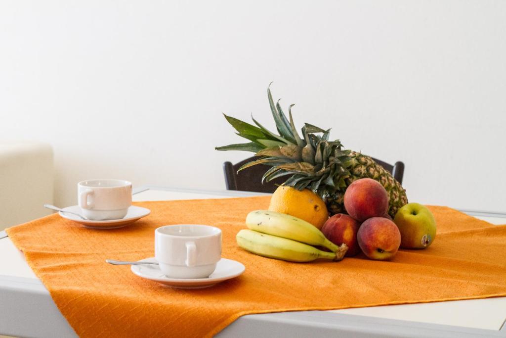 une assiette de fruits sur une table avec deux tasses dans l'établissement Club Esse Residence Capo D'orso, à Palau