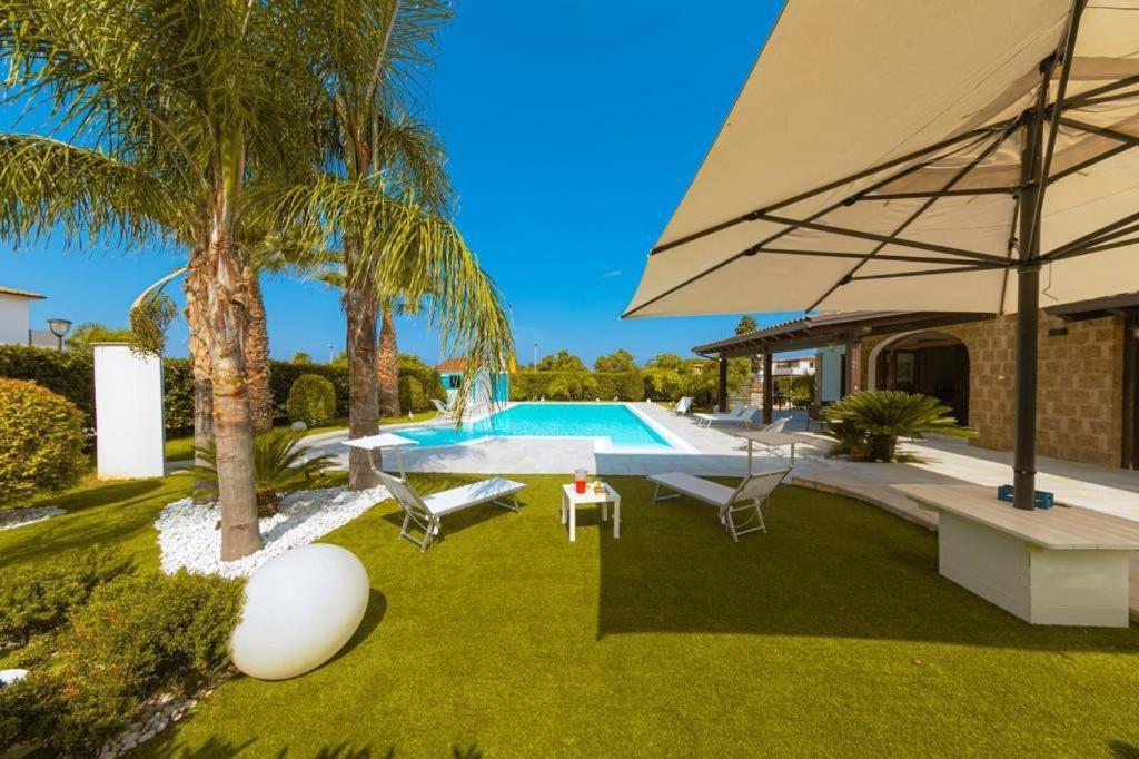 une arrière-cour avec une piscine et un grand parasol dans l'établissement Villa Oxidiana with pool and garden, à Campofelice di Roccella