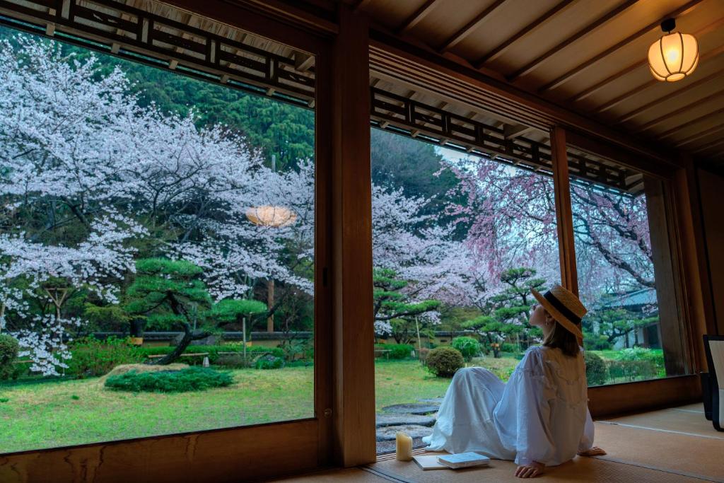 une femme assise dans une fenêtre donnant sur les arbres atakura dans l'établissement Oukai Villa Izumi, à Izumi