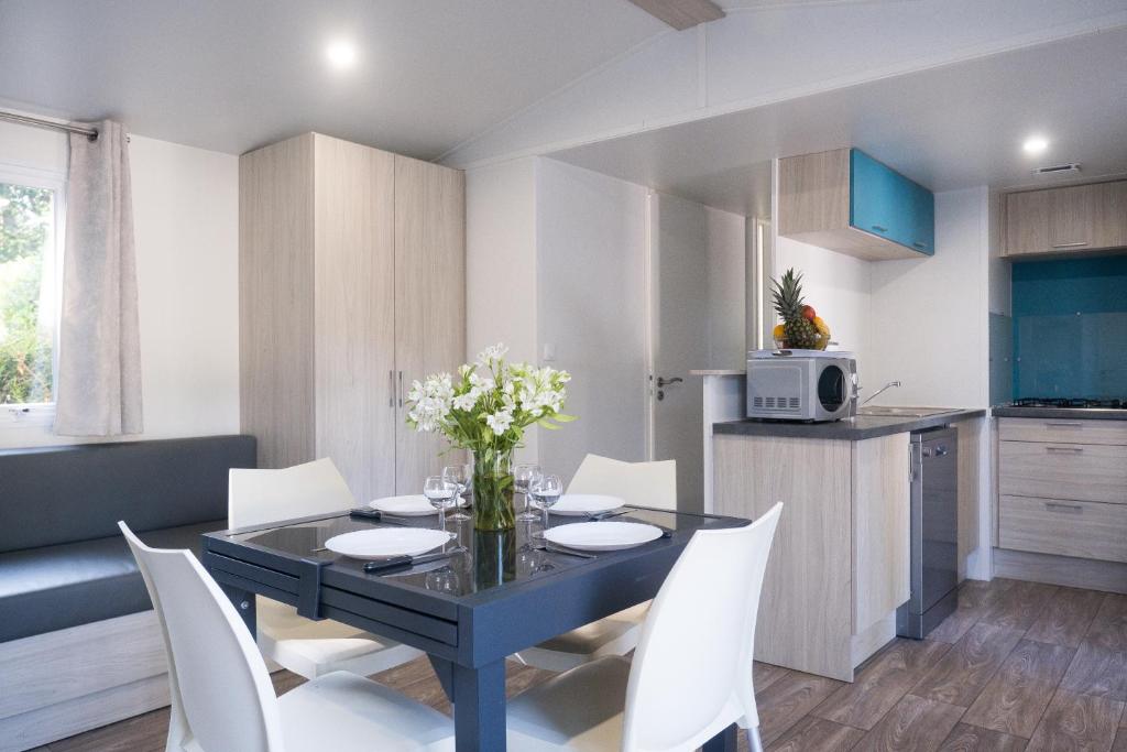 une cuisine et une salle à manger avec une table noire et des chaises blanches dans l'établissement Mobil Home XXL 4 chambres - Camping Country Park, à Touquin