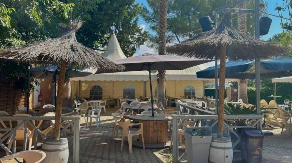 un patio avec des tables, des chaises et des parasols dans l'établissement Camping 2 étoiles - Piscine - ccb0fdi, à Villeneuve-lès-Maguelone