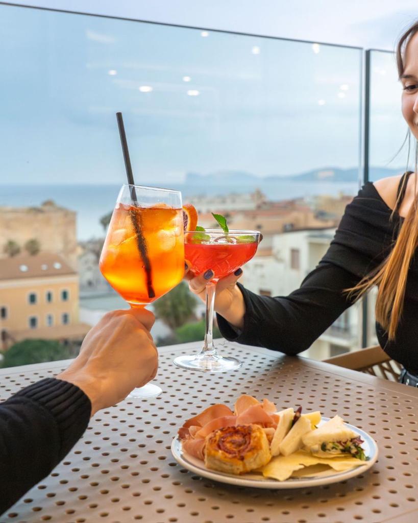deux personnes tenant des cocktails et une assiette de nourriture sur une table dans l'établissement Hotel La Margherita & SPA, à Alghero