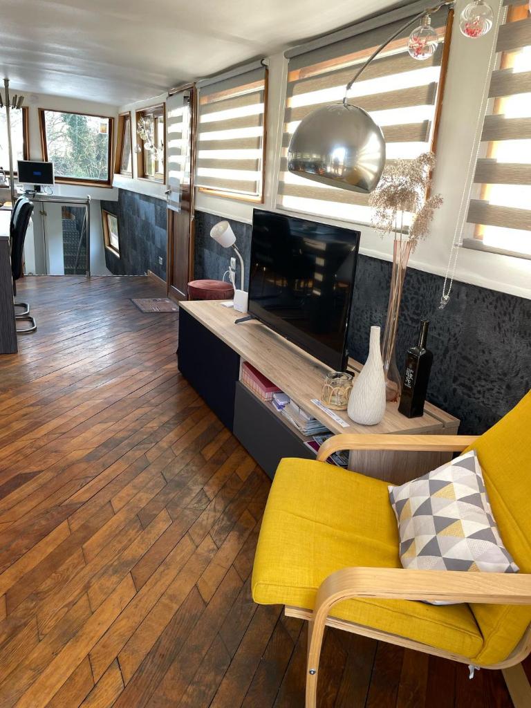 un salon avec une télévision et une chaise jaune dans l'établissement Nuit insolite à bord d'une péniche, 6 personnes, à Bergues