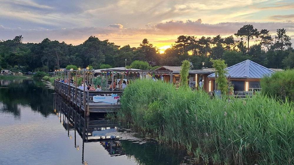 - un quai avec un bateau sur une rivière et un restaurant dans l'établissement ESCALE BASSIN- Mobile Home Lège Cap-Ferret - Village 4 étoiles LES VIVIERS, à Lège-Cap-Ferret