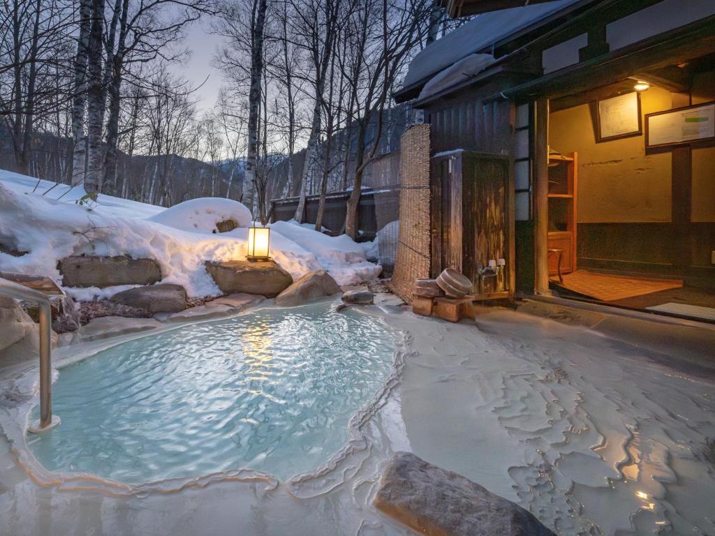 un bain à remous recouvert de neige à côté d'un bâtiment dans l'établissement Konashi No Yu Sasaya, à Matsumoto