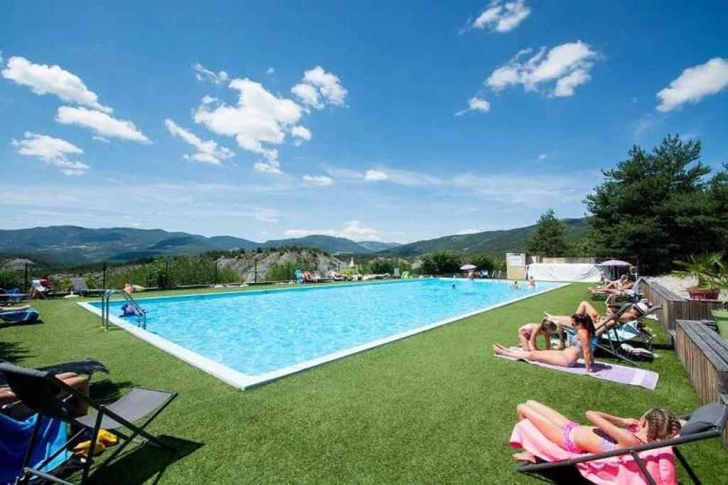 un groupe de personnes se posant sur l'herbe près d'une piscine dans l'établissement Camping 4 étoiles - Piscine - ccbacgb, à Rosans