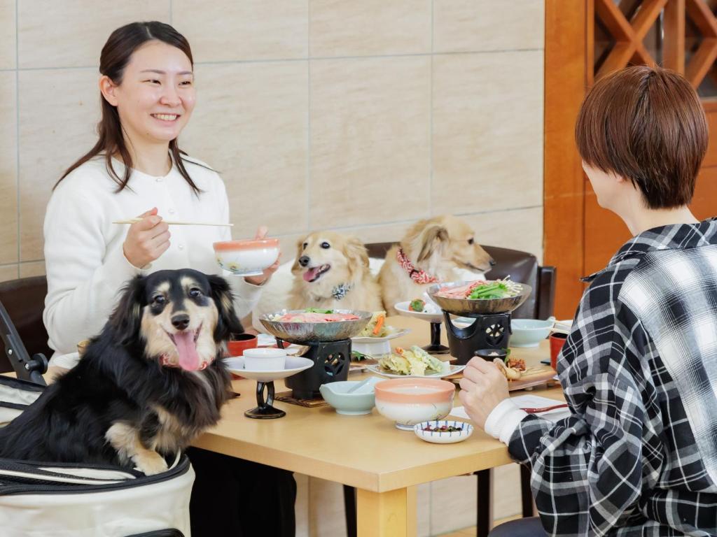 une femme et deux chiens assis à une table avec de la nourriture dans l'établissement KAMENOI HOTEL SHIOBARA Dog Friendly Hotel, à Nasushiobara