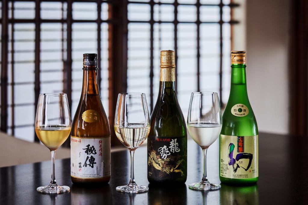 3 bouteilles de vin et 4 verres à vin sur une table dans l'établissement NIPPONIA HOTEL Takehara Saltworks Town, à Takekara