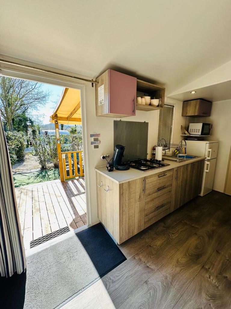 une cuisine avec des placards en bois et une porte donnant sur une terrasse. dans l'établissement Mobilhome 228 proche du Lac , Tv , clim ect Camping, à La Roque-dʼAnthéron