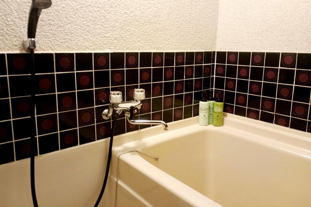 La salle de bains est pourvue d'une baignoire et de carrelage noir. dans l'établissement Ryokan Wataya, à Karatsu